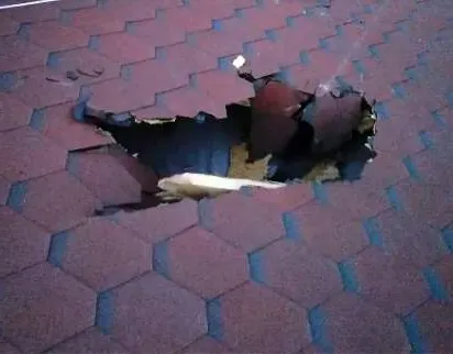 Пролом с рваными краями в кровле из гибкой черепицы, требующий аварийного ремонта
