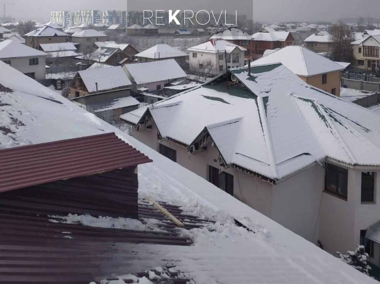 Заснеженные скаты новой кровли из профнастила, рядом дом с вальмовой крышей