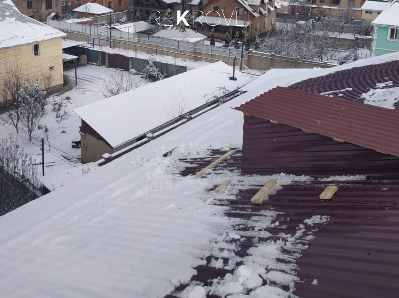 Укладка бордового профнастила на крыше частного дома зимой, вид сверху