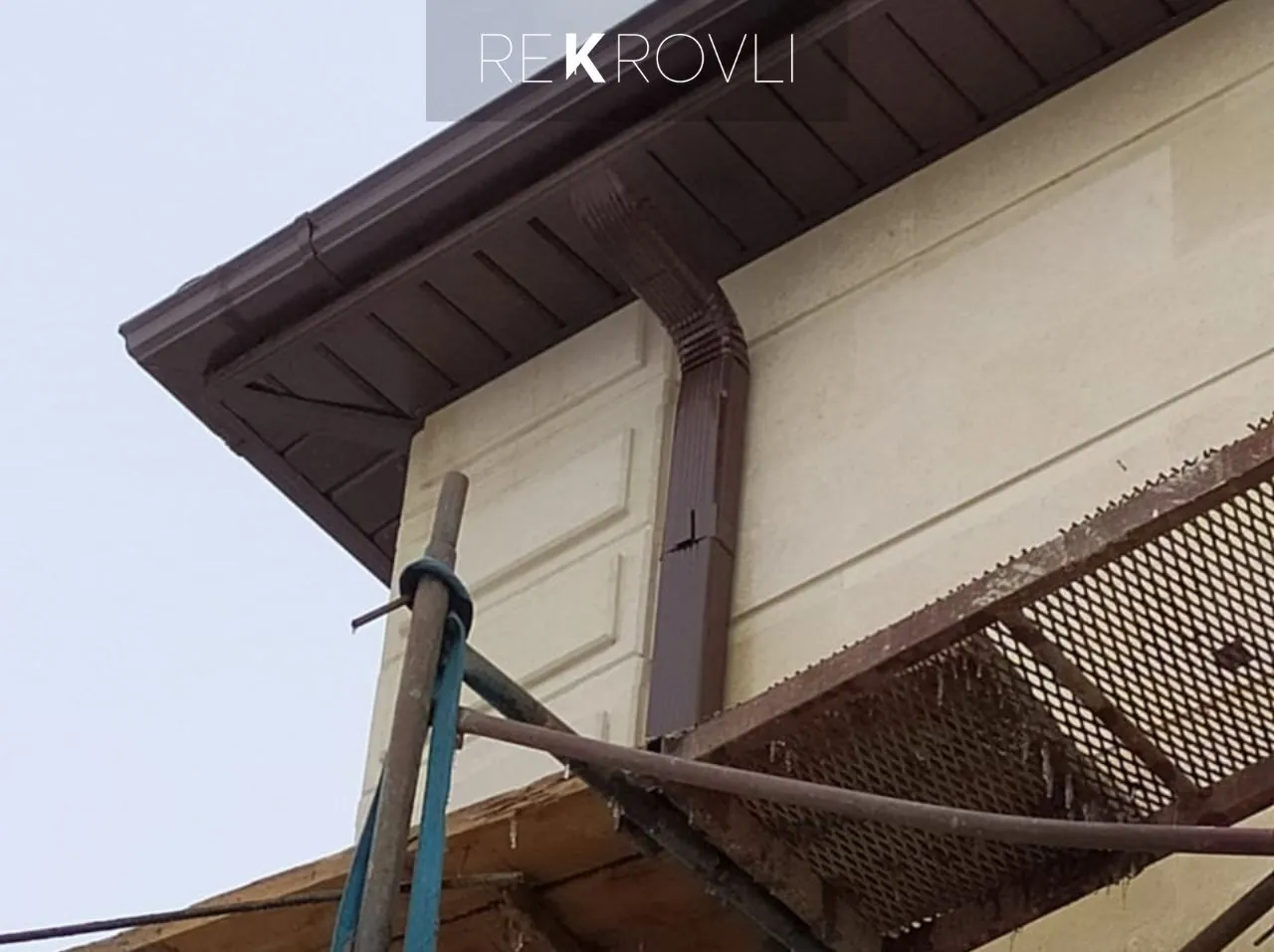 Подшивка карниза софитами и монтаж коричневой водосточной трубы на частном доме