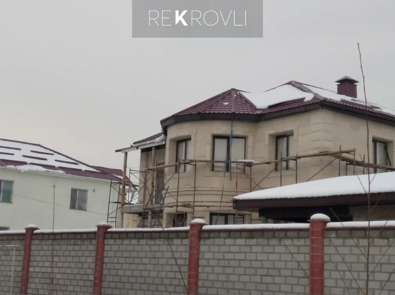Бордовая металлочерепица на вальмовой крыше двухэтажного дома с эркером, идёт отделка фасада