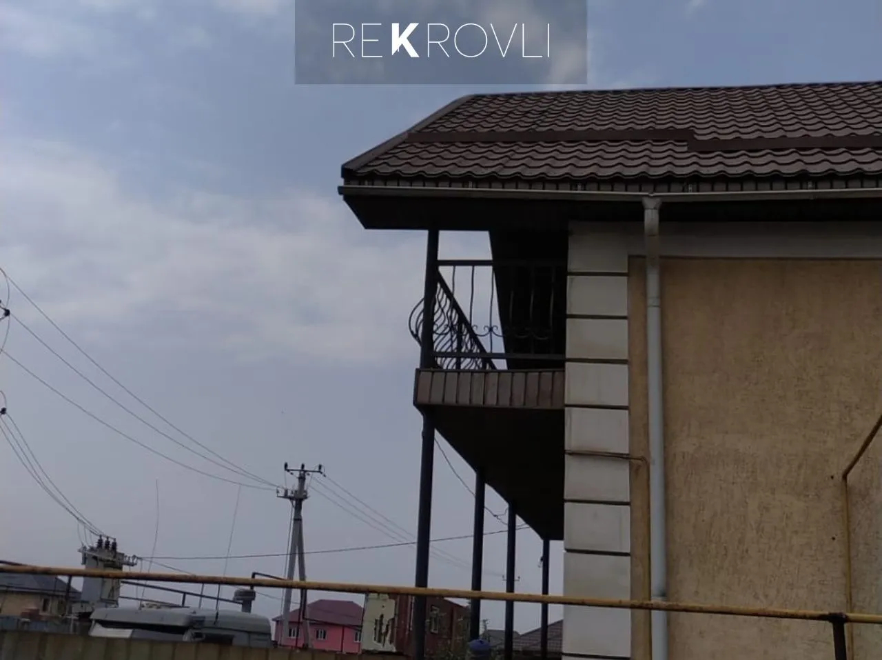 Свес крыши из коричневой металлочерепицы с подшивкой и водосточной трубой на двухэтажном доме